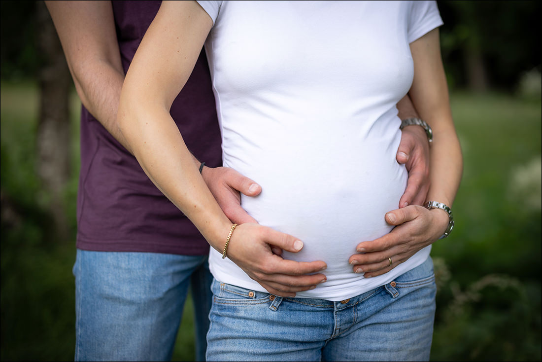  Detailaufnahme von Händen auf dem Babybauch während eines Outdoor Shootings im Schwarzwald.